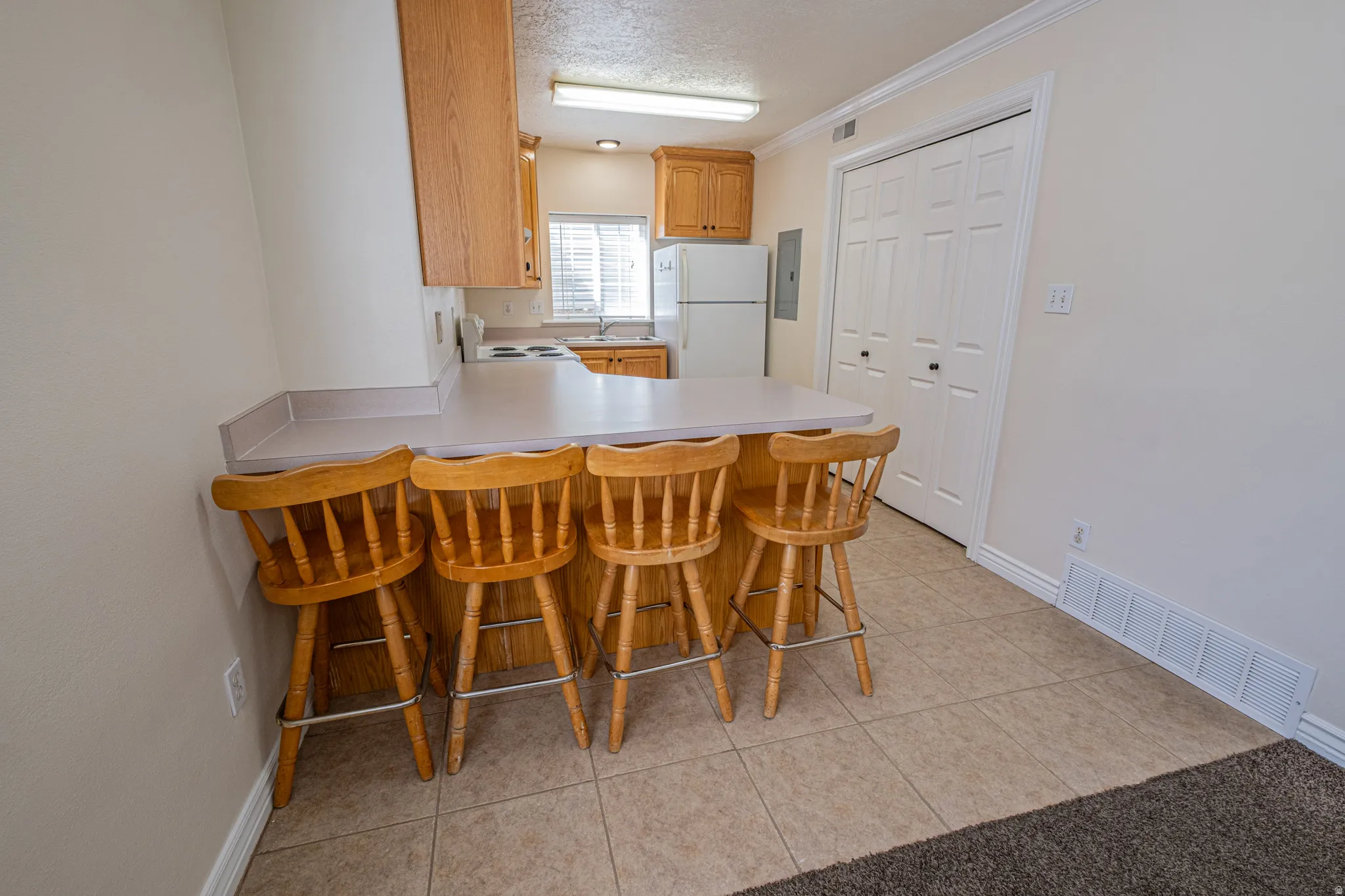 Kitchen featuring a textured ceiling, a kitchen breakfast bar, white appliances, light tile patterned floors, and light countertops