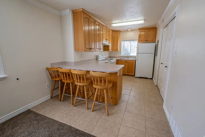Kitchen featuring a peninsula, white appliances, a textured ceiling, light countertops, and a kitchen bar