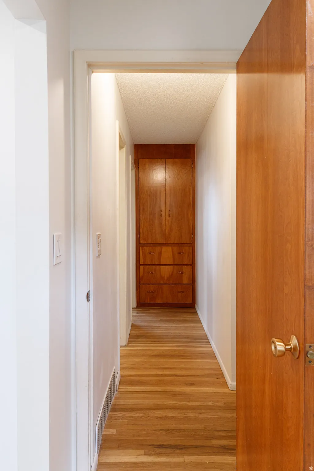 Hallway with light wood-type flooring and a textured ceiling