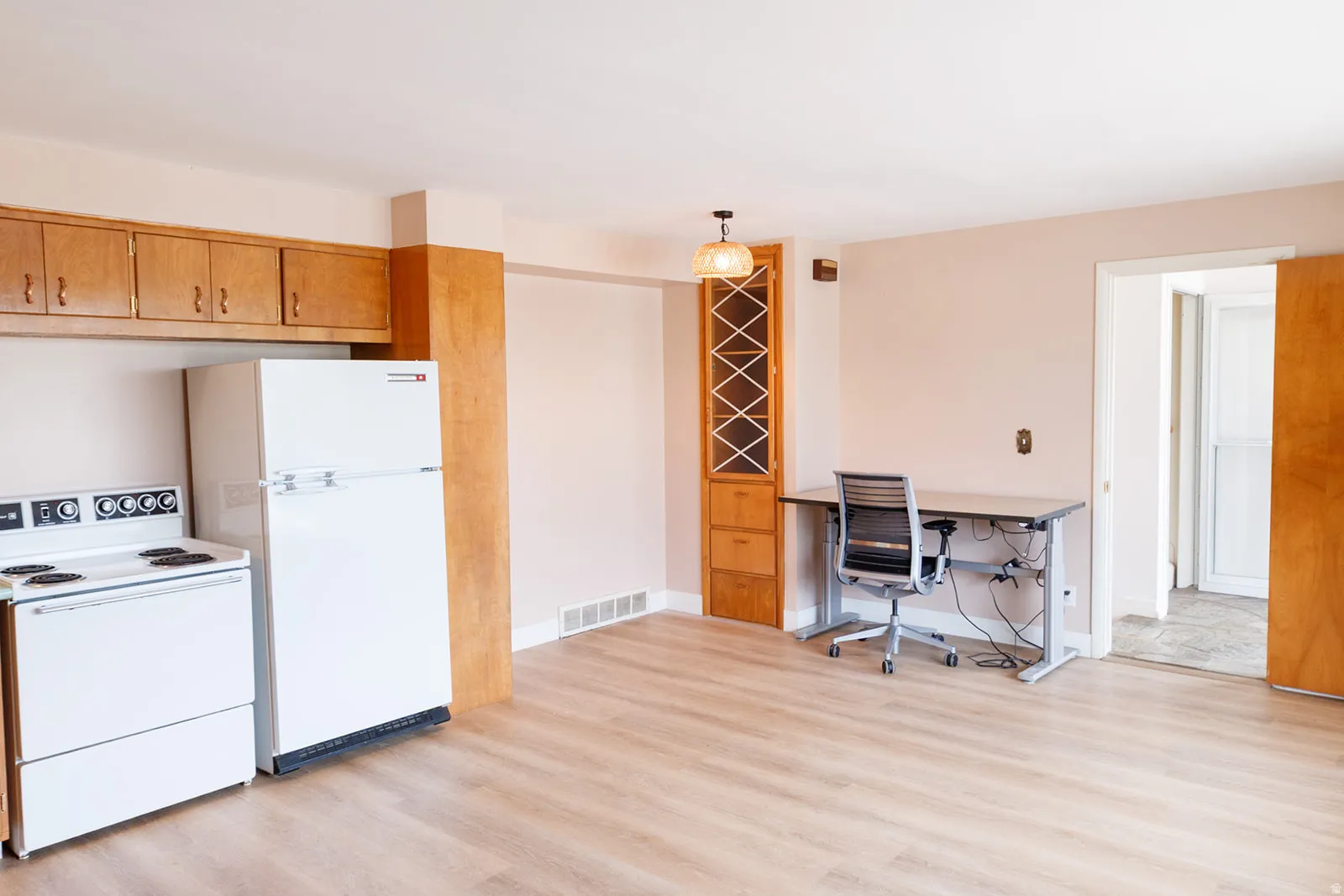Kitchen featuring white appliances, light wood finished floors, a desk, wood finish cabinetry, and light countertops