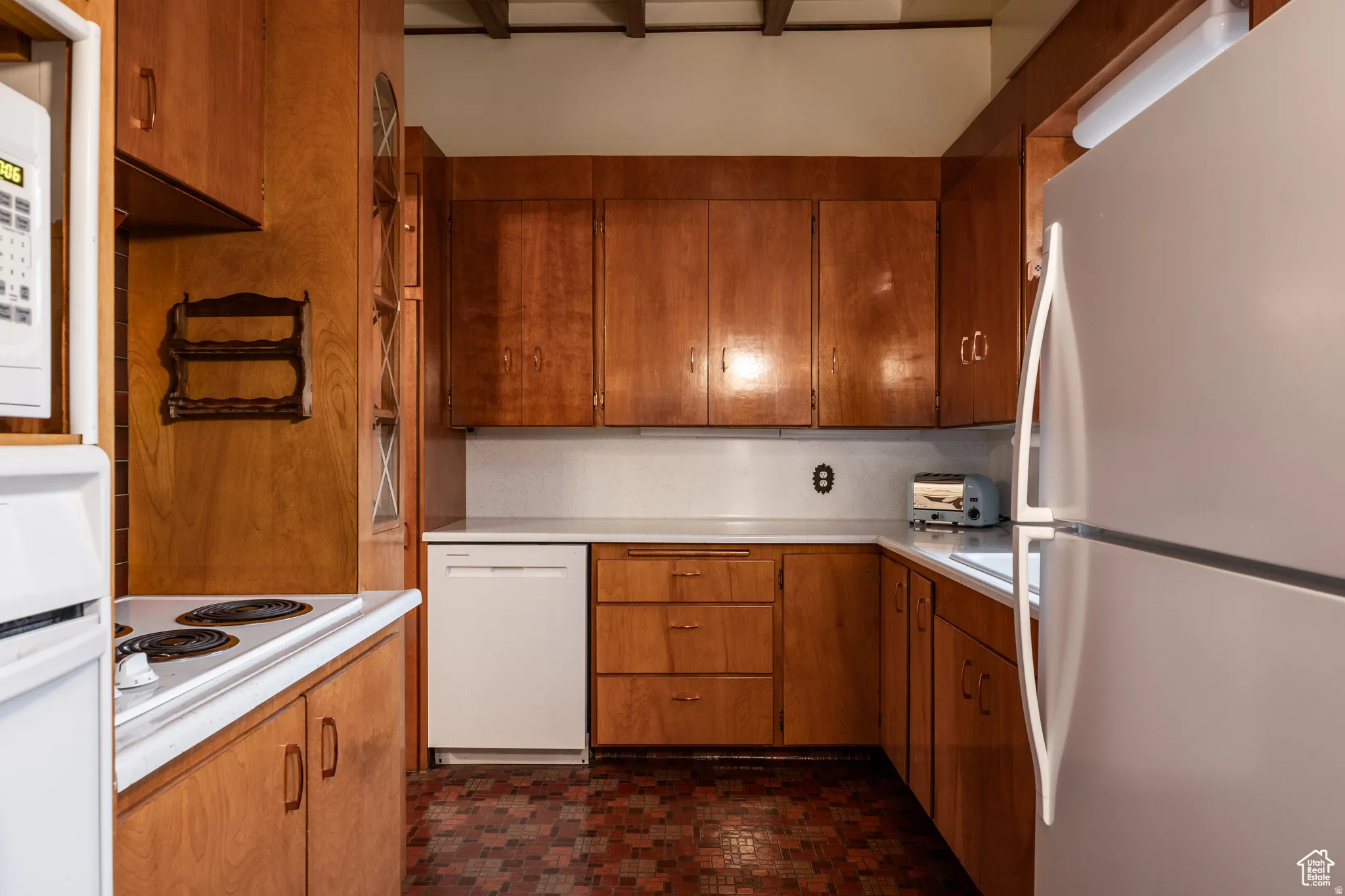 Kitchen with white appliances, wood finish cabinetry, light countertops, and brick patterned floors