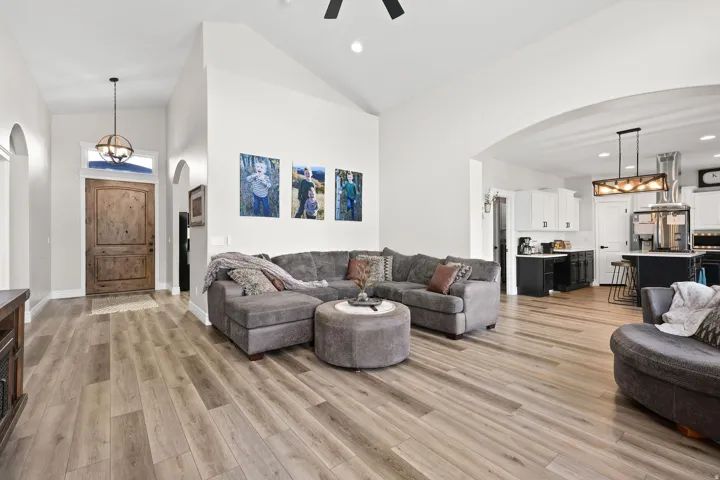 Living room featuring arched walkways, hanging lights, a ceiling fan, light wood finished floors, and vaulted ceiling