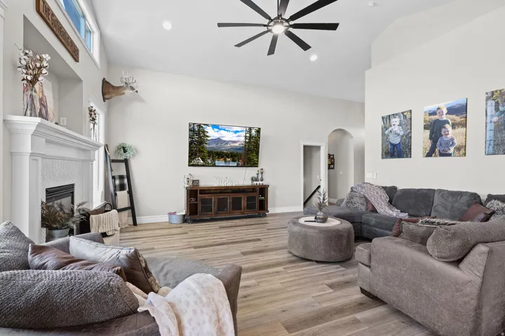 Living room with a high ceiling, arched walkways, light wood-type flooring, ceiling fan, and a glass covered fireplace