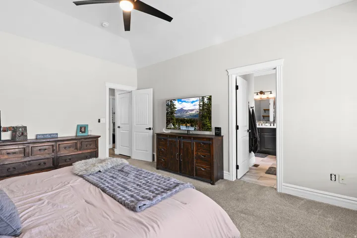 Bedroom with light carpet, a ceiling fan, lofted ceiling, and ensuite bathroom