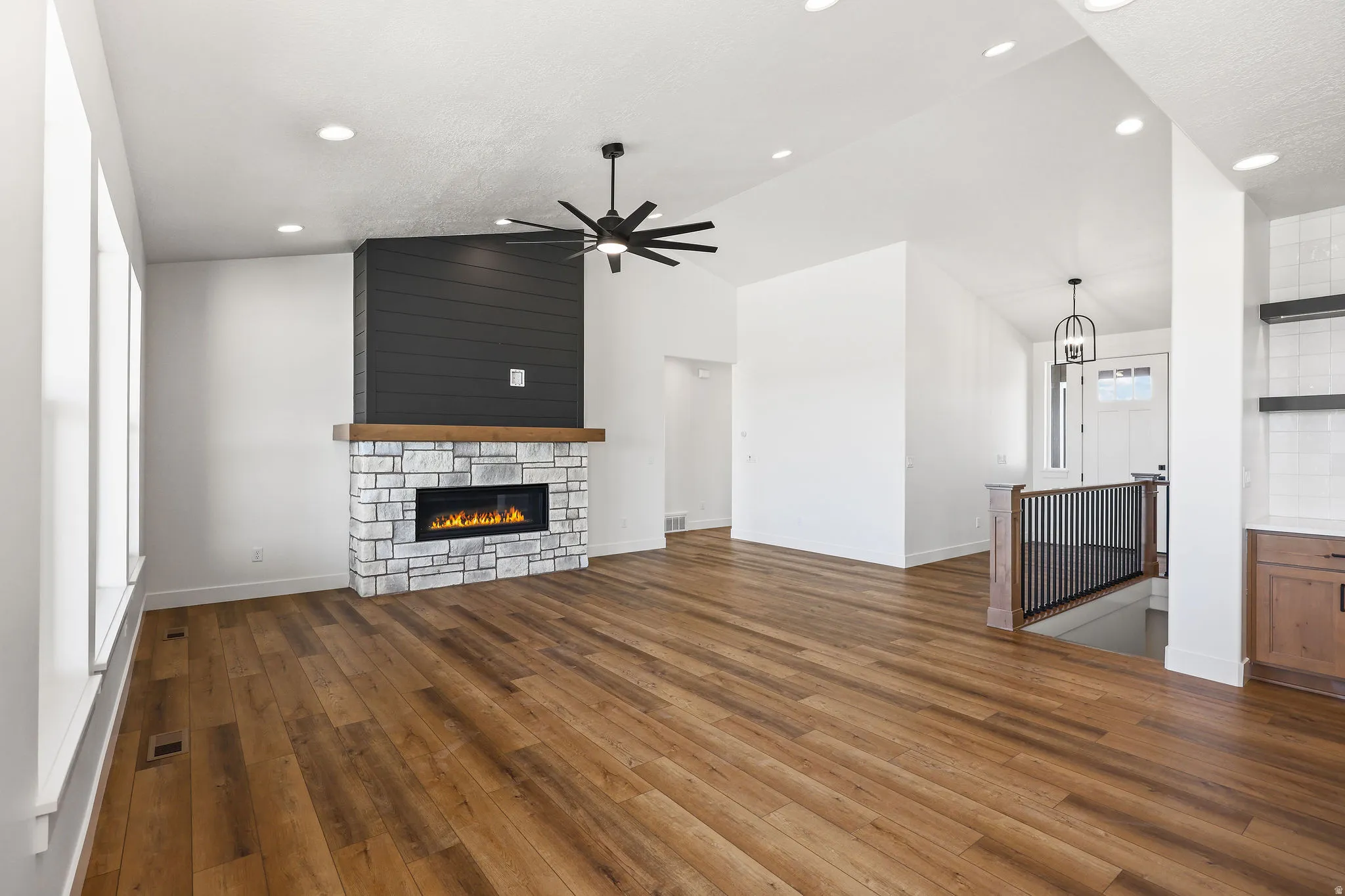 Unfurnished living room featuring a fireplace, dark wood finished floors, lofted ceiling, a ceiling fan, and suspended lighting
