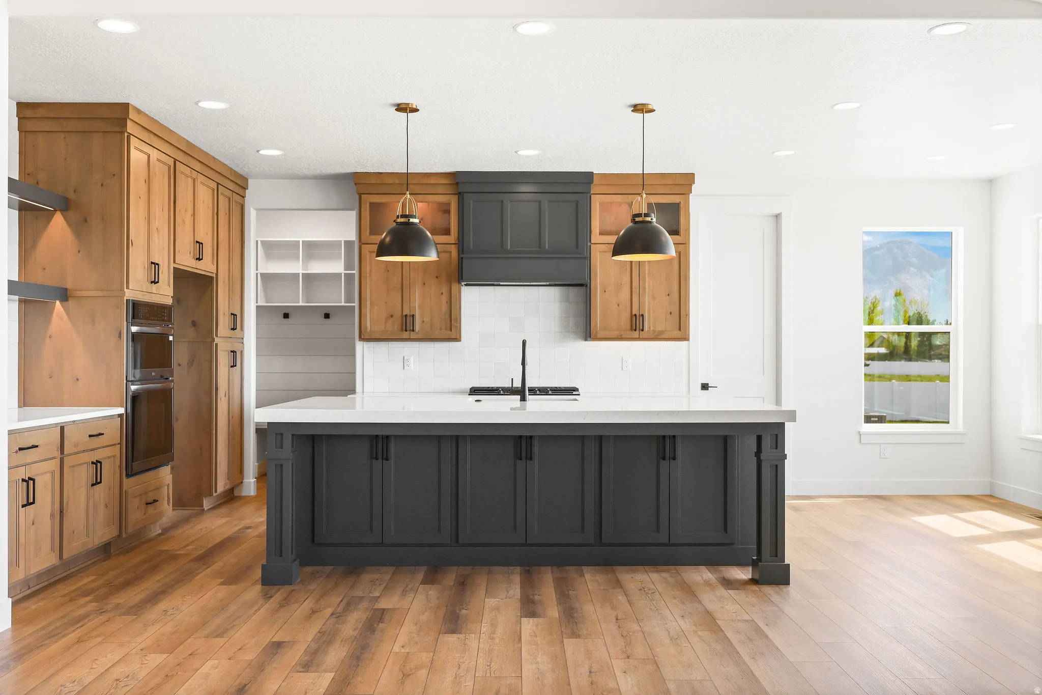 Two tone kitchen with two tone cabinetry, an island with sink, light wood-style floors, double oven, and tasteful backsplash