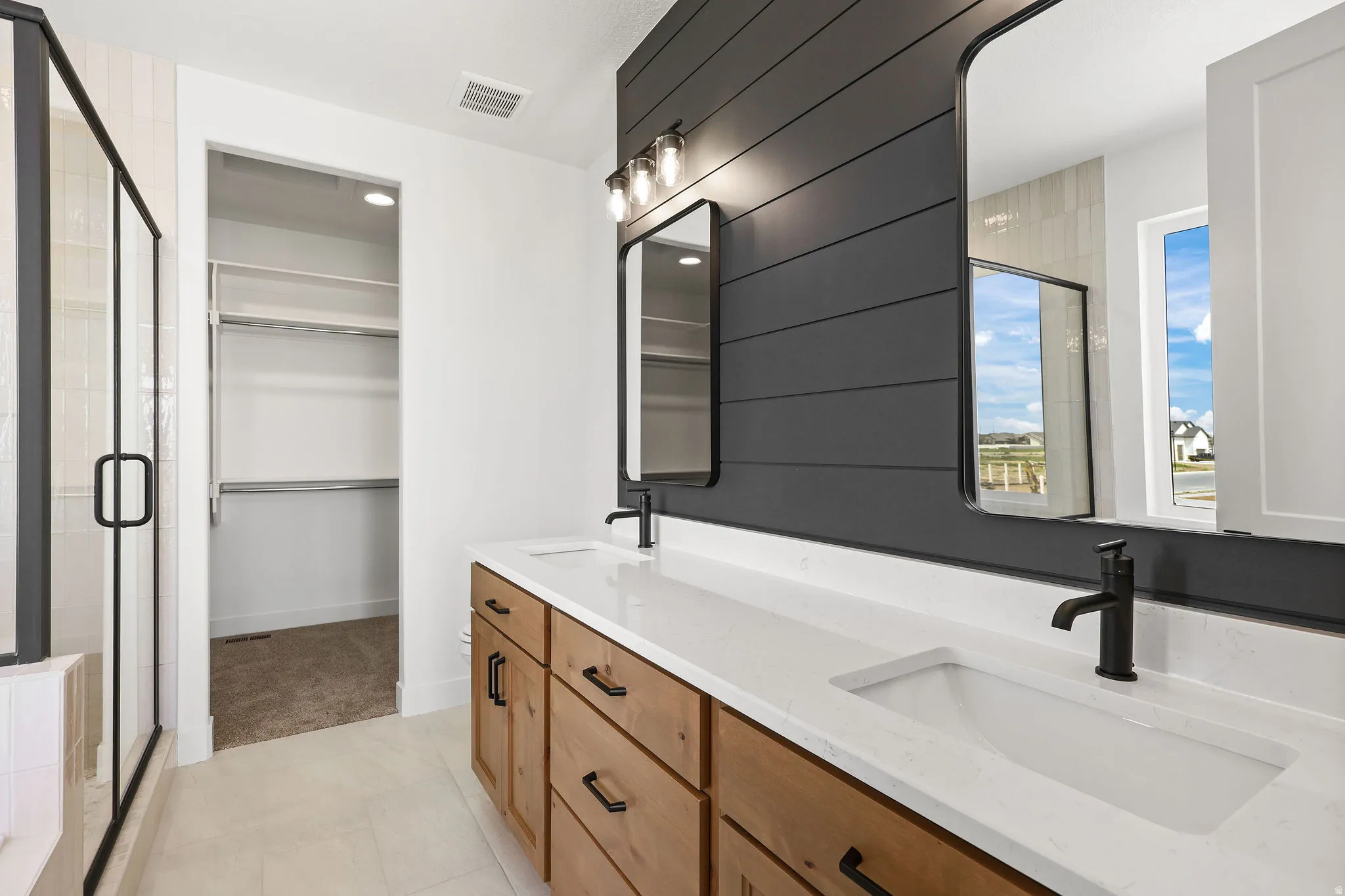 Bathroom with double vanity, a stall shower, a spacious closet, and light tile patterned floors