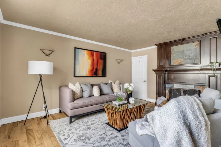 Living room with light wood-type flooring, ornamental molding, a tiled fireplace, and a textured ceiling
