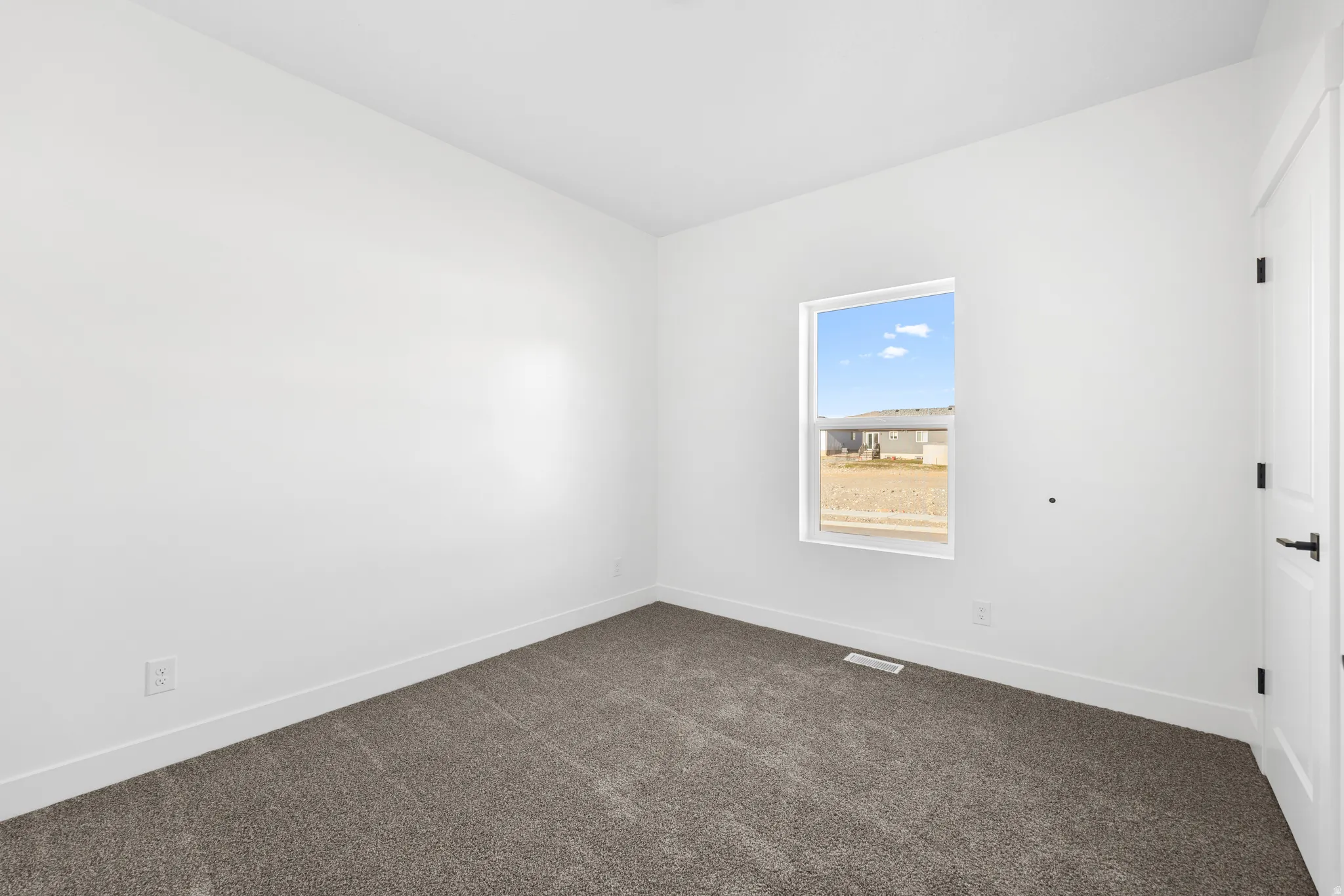 Spare room featuring dark carpet and baseboards