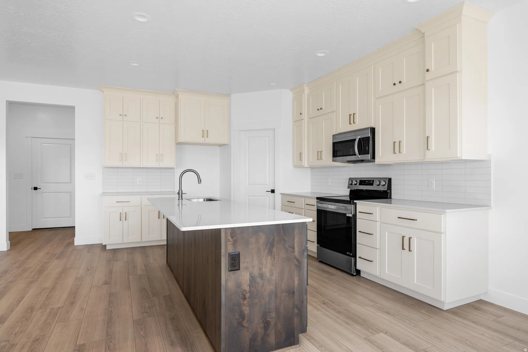 Dual tone kitchen featuring stainless steel appliances, dual tone cabinets, light stone countertops, a kitchen island with sink, and backsplash
