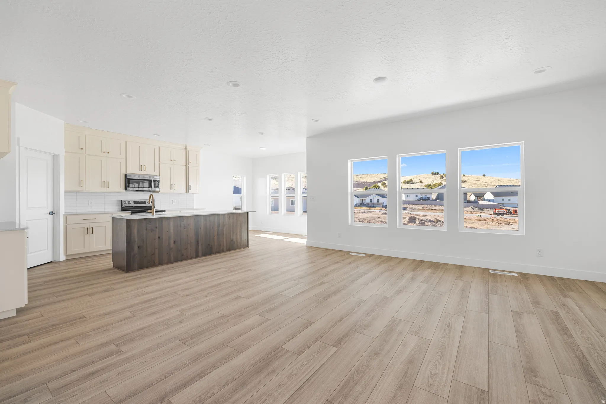 Dual tone kitchen with open floor plan, a kitchen island with sink, decorative backsplash, light wood-type flooring, and stainless steel appliances