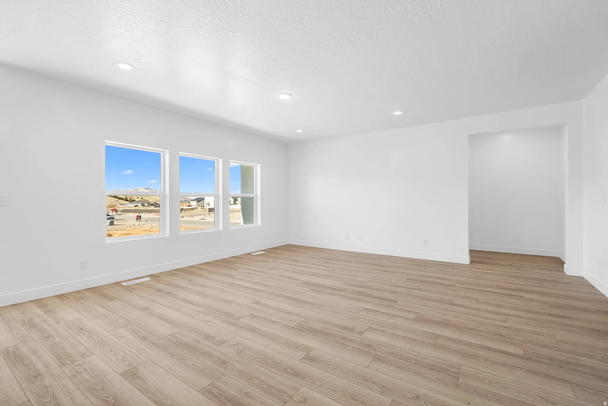 Empty room with light wood-type flooring, a textured ceiling, and recessed lighting