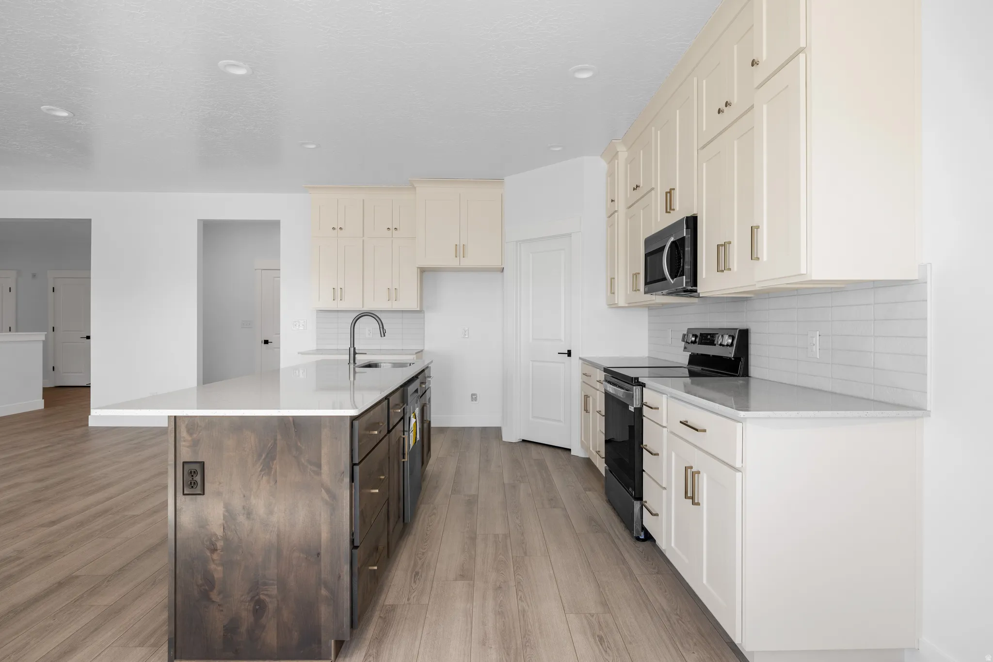 Kitchen with dual tone cabinets, stainless steel appliances, light stone countertops, an island with sink, and light wood-style flooring