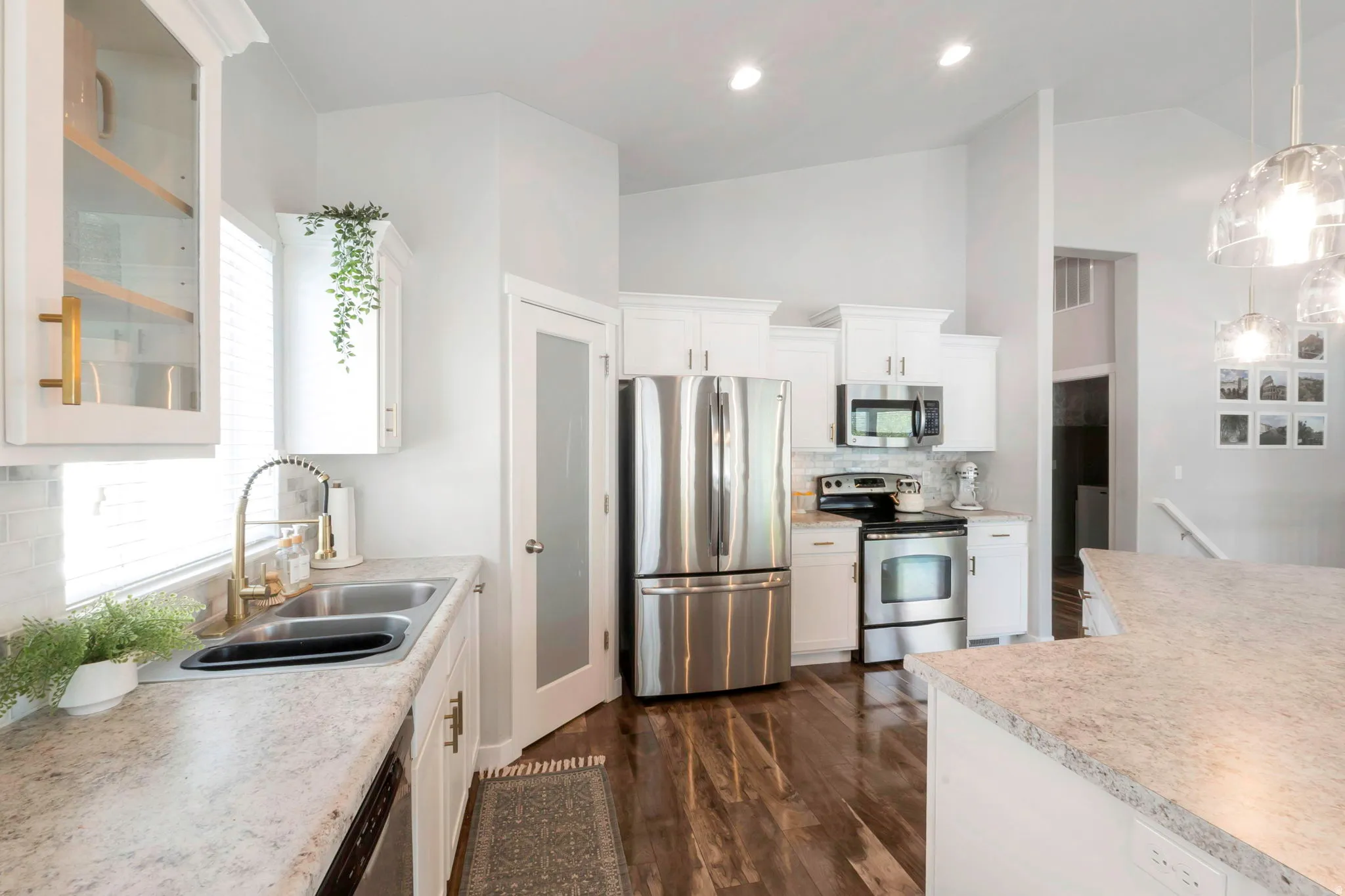 Kitchen with stainless steel appliances, glass fronted cabinets, white cabinets, decorative light fixtures, and light countertops