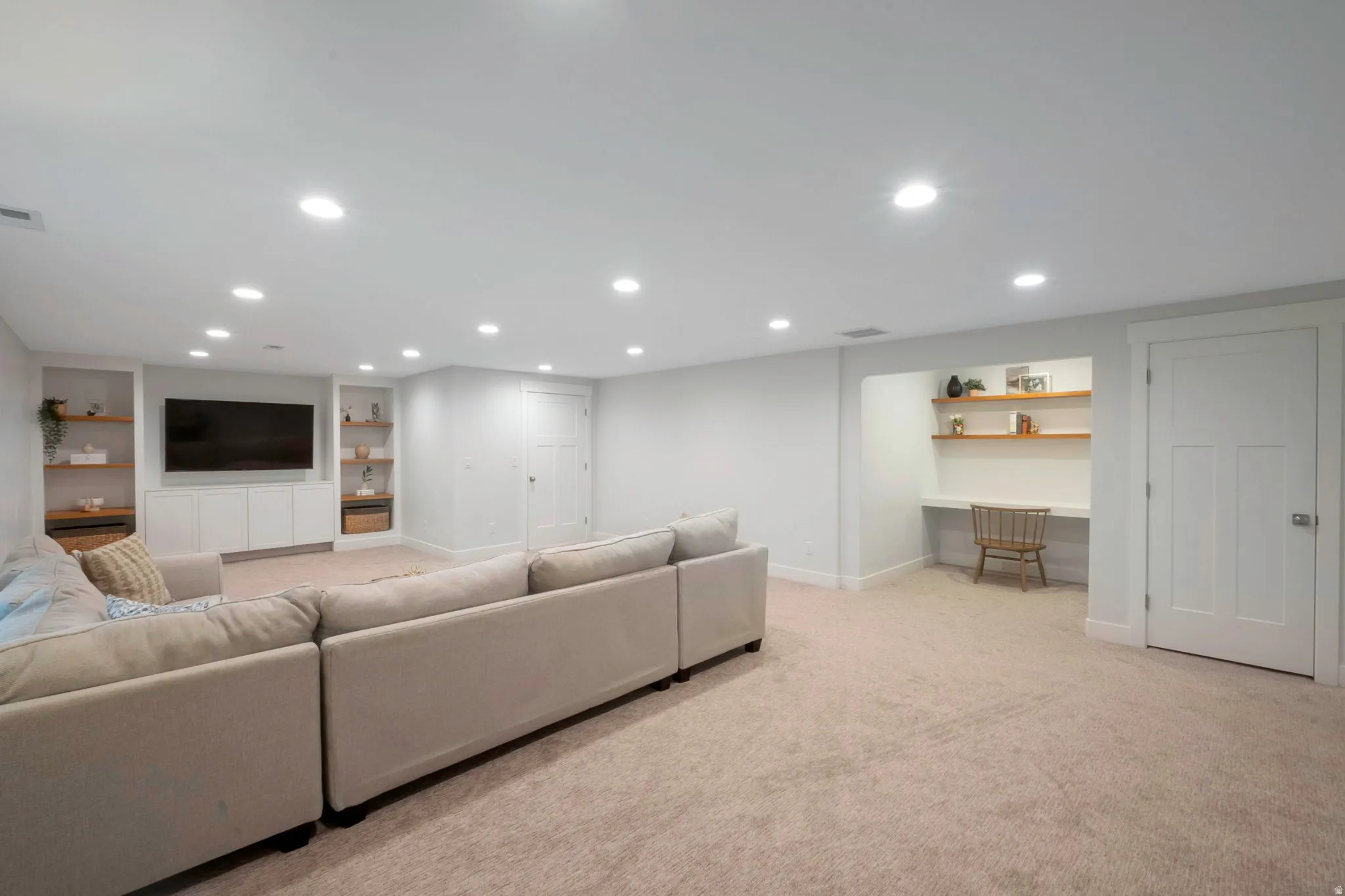 Living area with built in shelves, light carpet, and recessed lighting