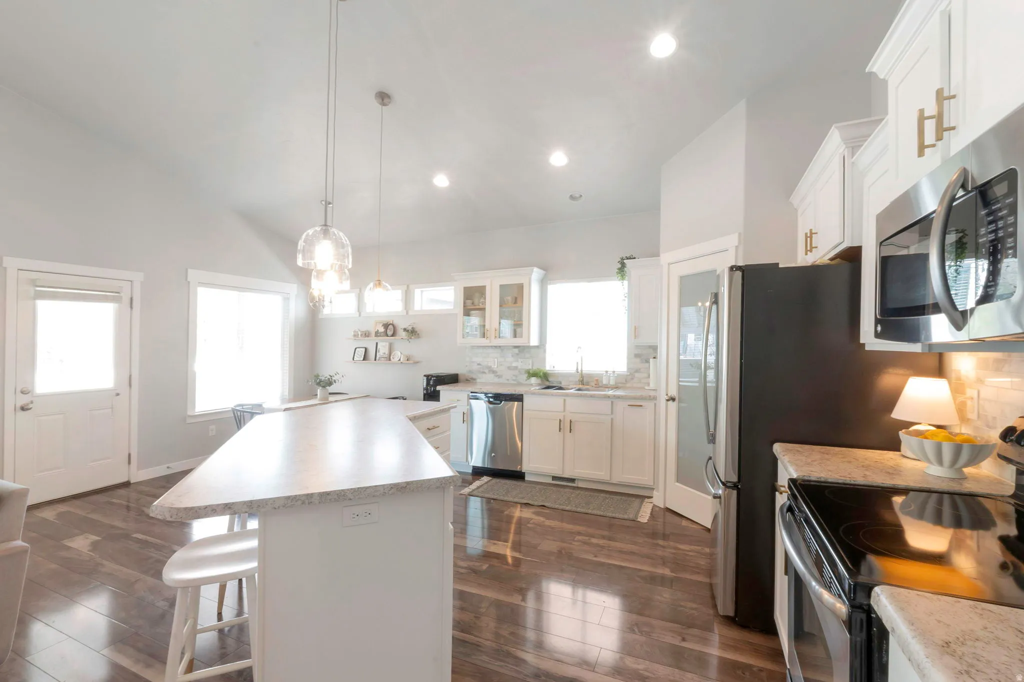 Kitchen with stainless steel appliances, decorative backsplash, light countertops, white cabinets, and a breakfast bar