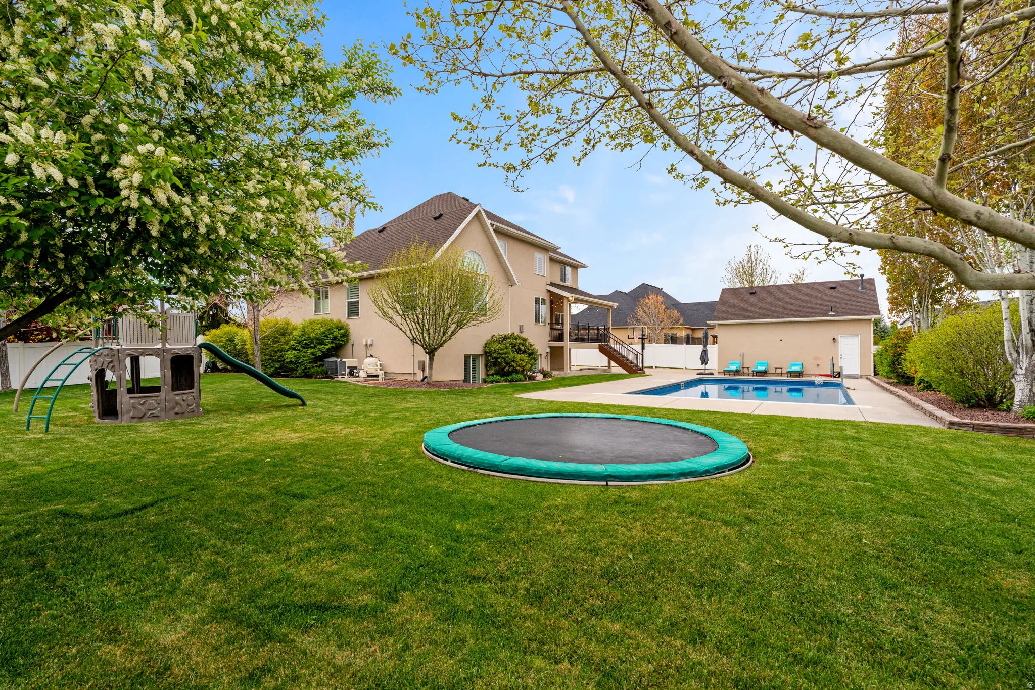 Back of property featuring a patio area, a playground, an outdoor pool, stucco siding, and a trampoline