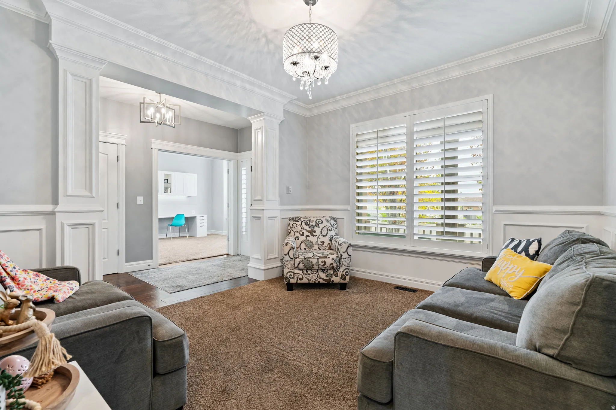 Living area featuring decorative columns, crown molding, a chandelier, a decorative wall, and a wainscoted wall