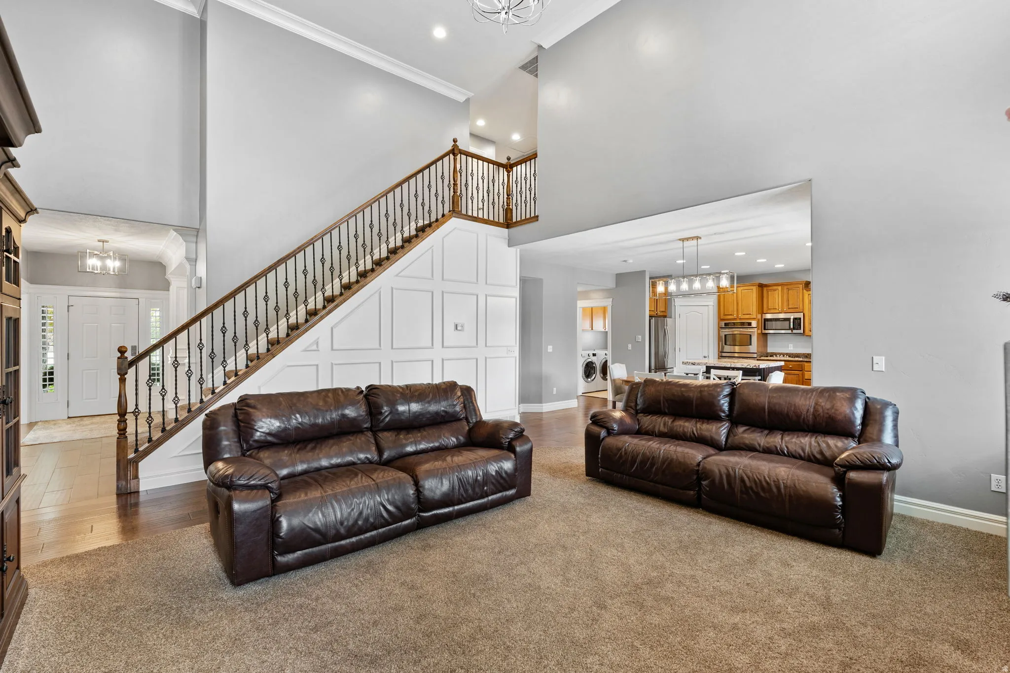 Living area featuring a chandelier, ornamental molding, a high ceiling, washer / dryer, and light colored carpet