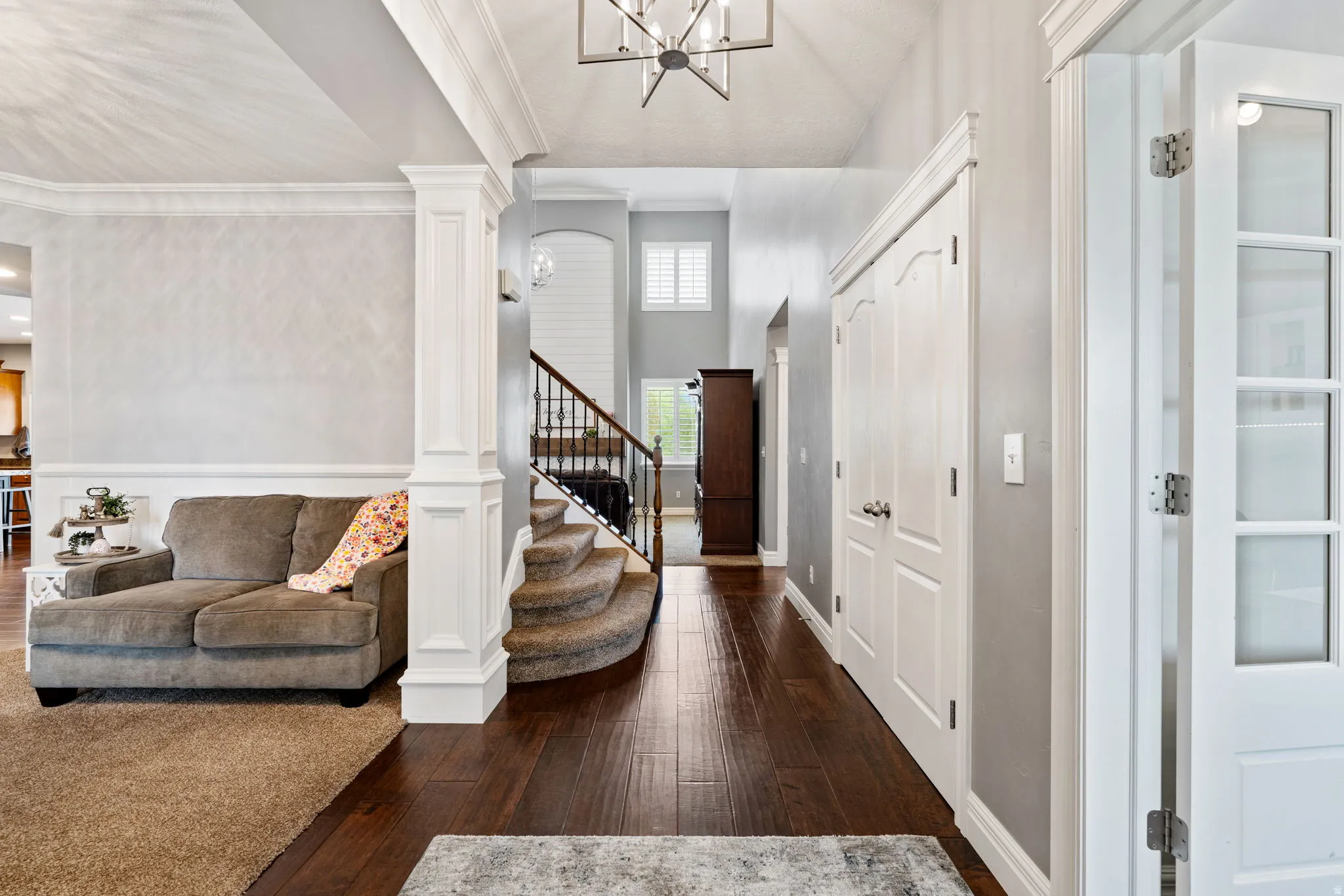 Foyer entrance featuring dark wood-type flooring, a chandelier, ornamental molding, and decorative columns