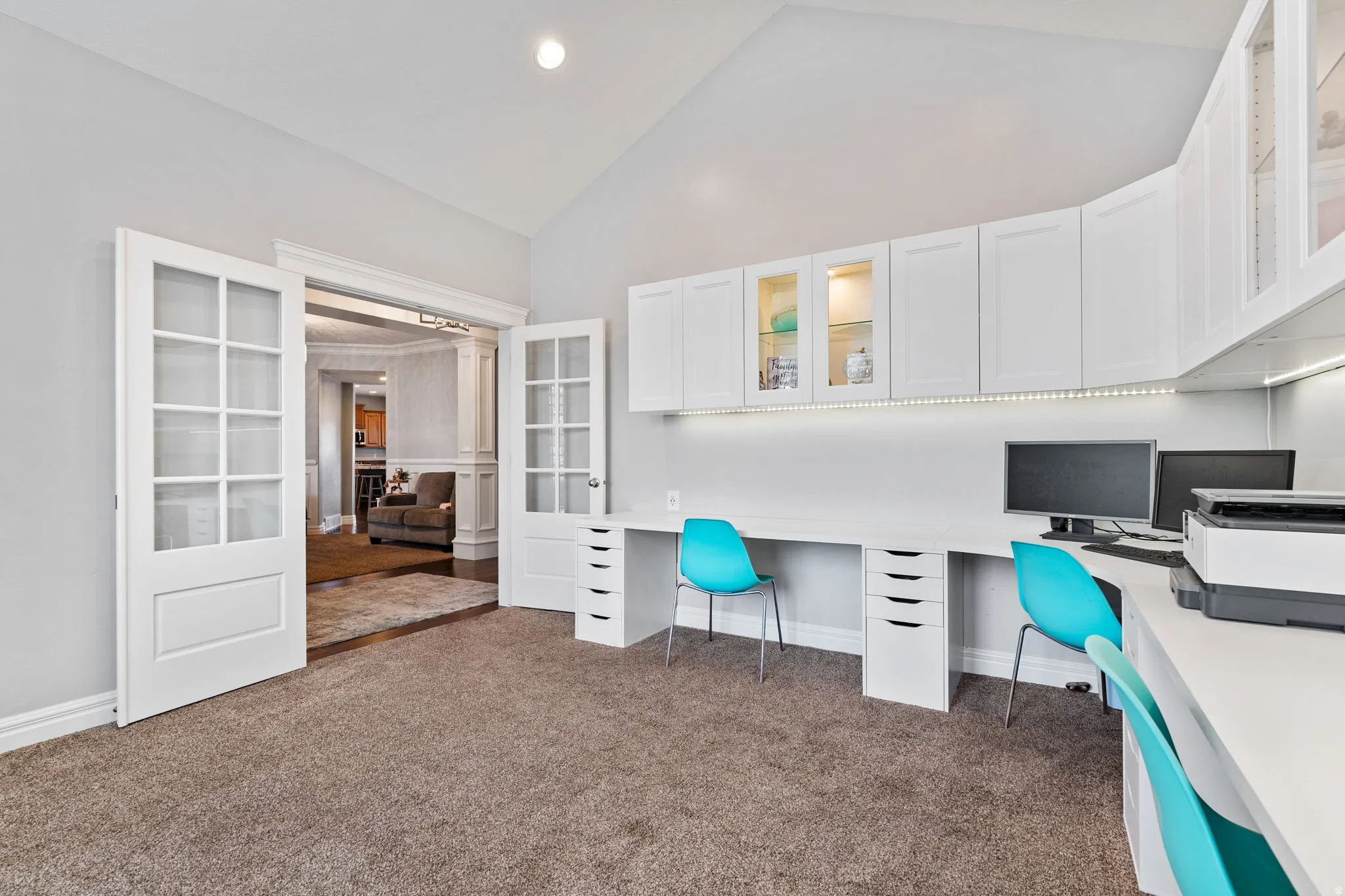 Office space featuring lofted ceiling, built in desk, dark carpet, french doors, and recessed lighting