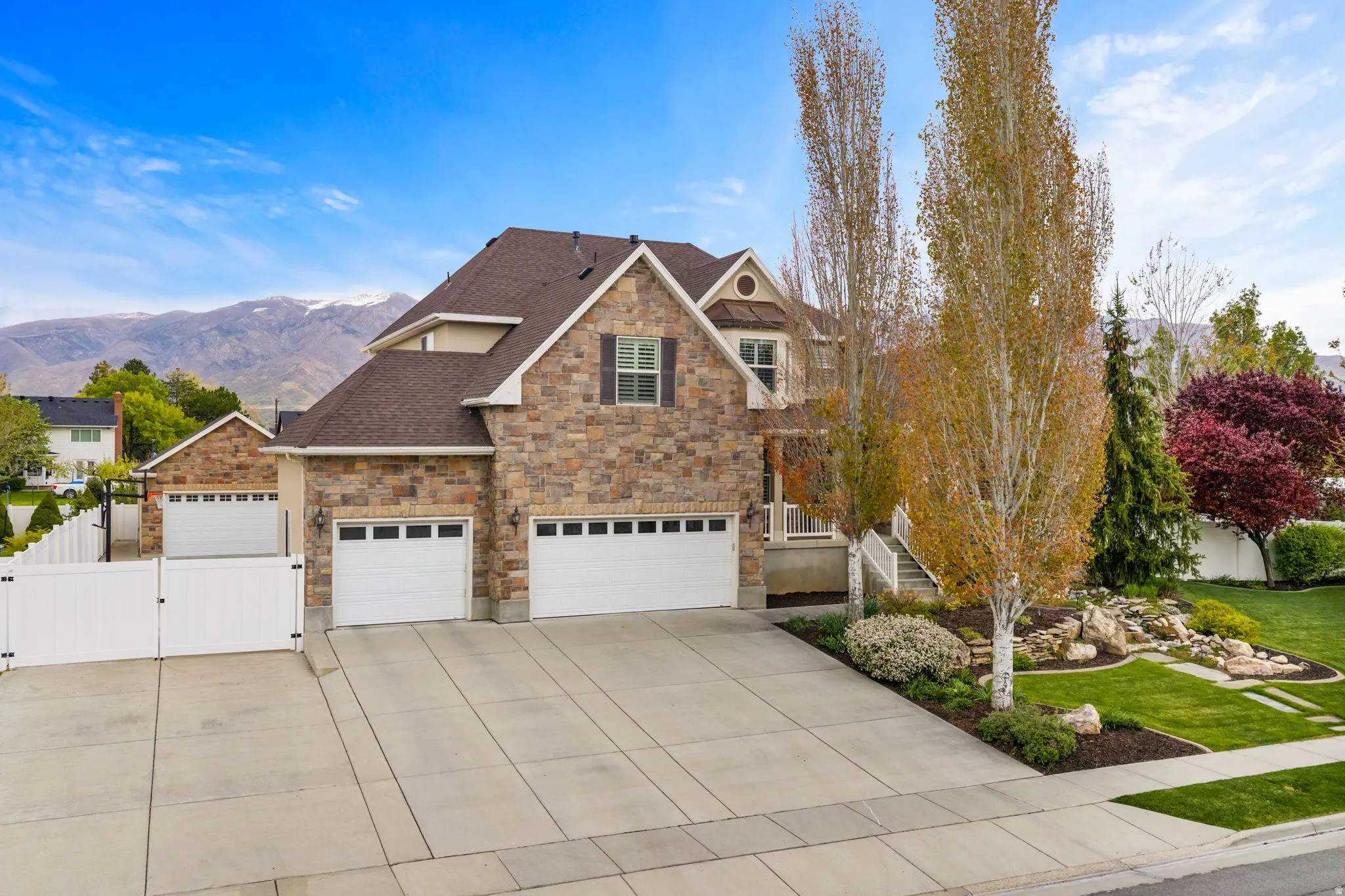 View of front facade featuring a gate, stone siding, a shingled roof, and driveway