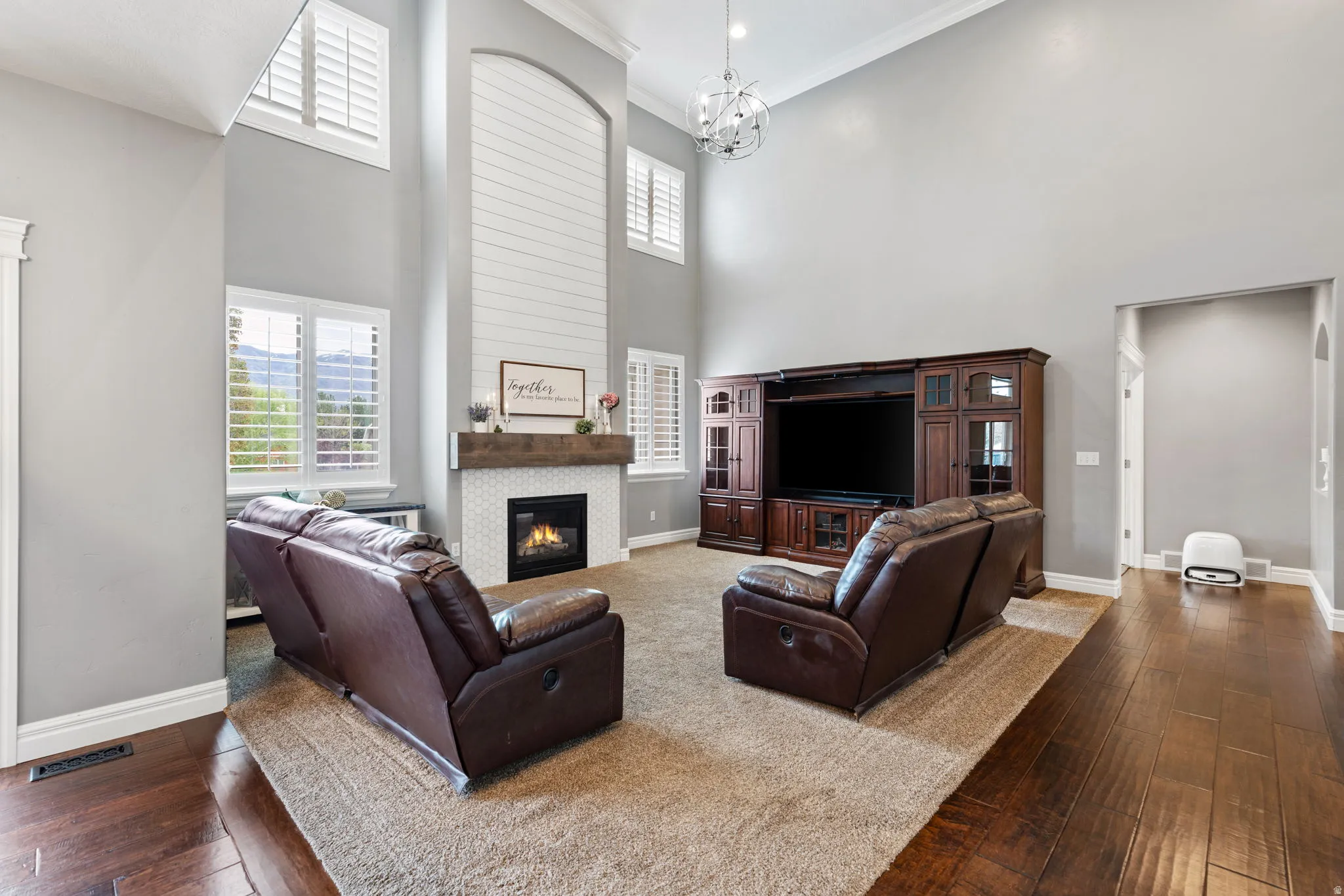 Living area featuring a high ceiling, dark wood-type flooring, crown molding, healthy amount of natural light, and a large fireplace