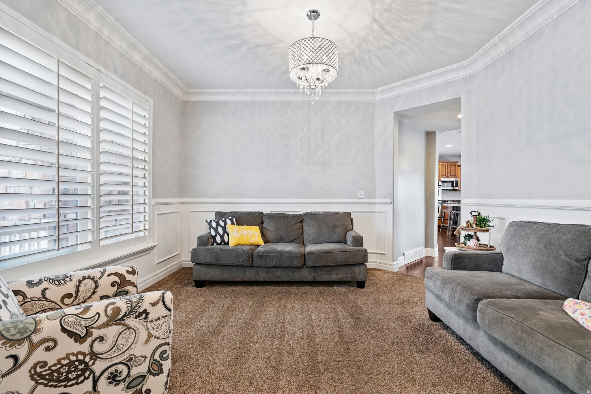Living room with ornamental molding, a decorative wall, wainscoting, a chandelier, and dark colored carpet