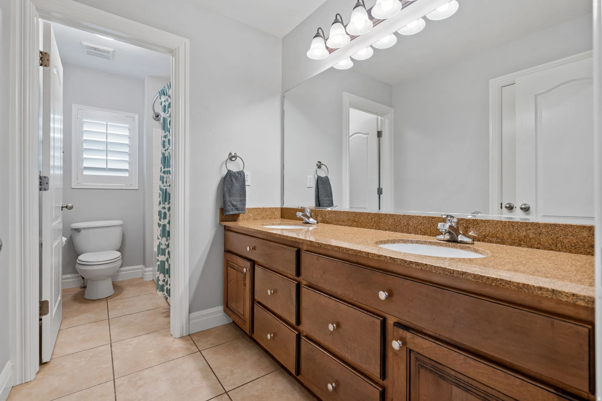 Bathroom featuring double vanity, curtained shower, and light tile patterned flooring
