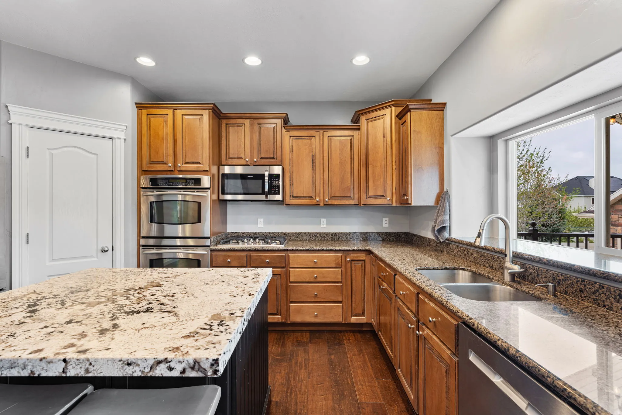 Kitchen with stainless steel appliances, light stone countertops, wood finish cabinetry, recessed lighting, and dark wood-style flooring