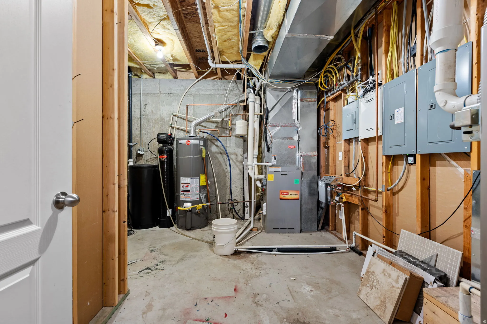 Utility room featuring electric panel, strapped water heater, and heating unit
