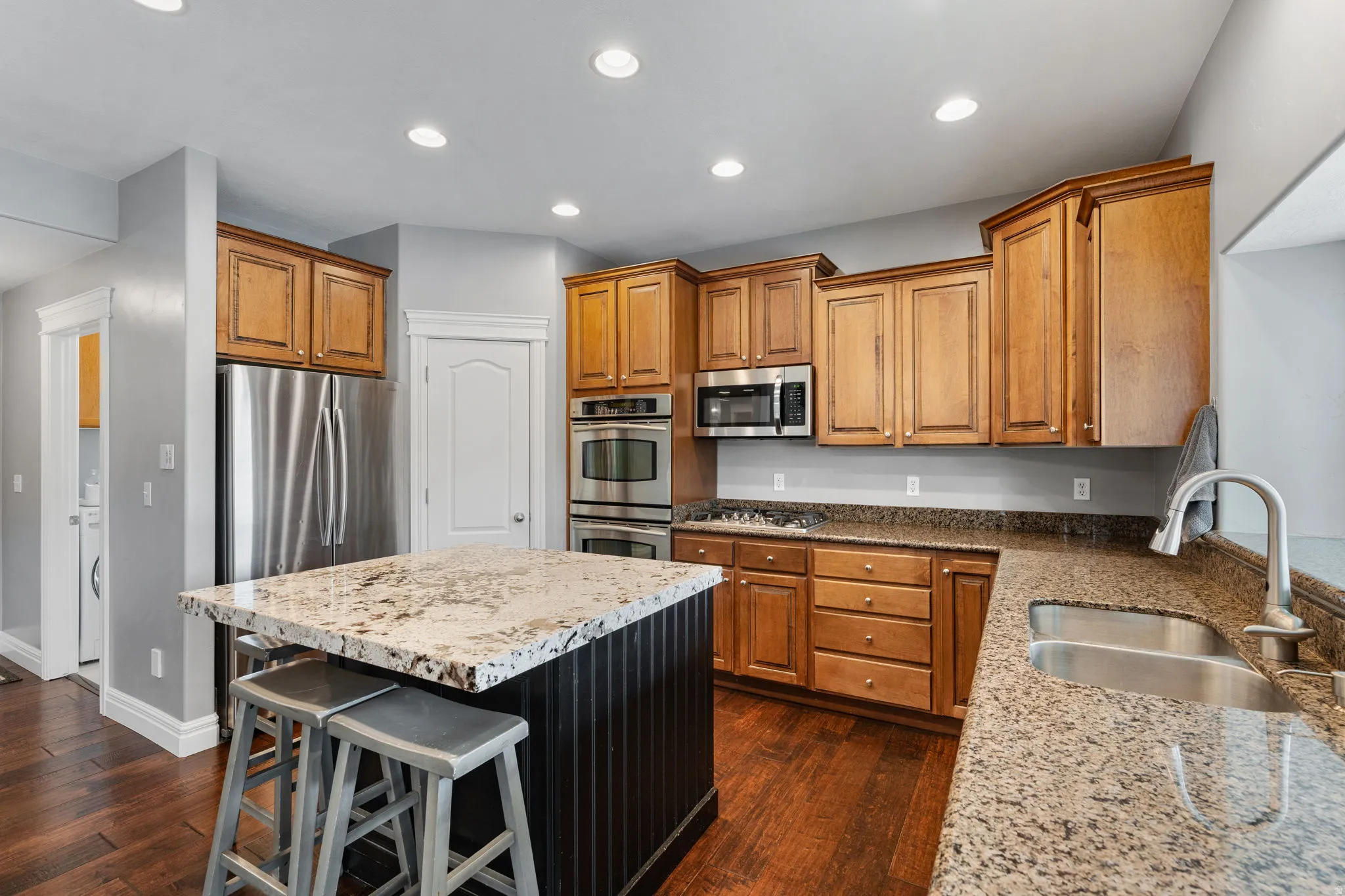 Kitchen with light stone countertops, a kitchen breakfast bar, stainless steel appliances, a center island, and wood finish cabinetry