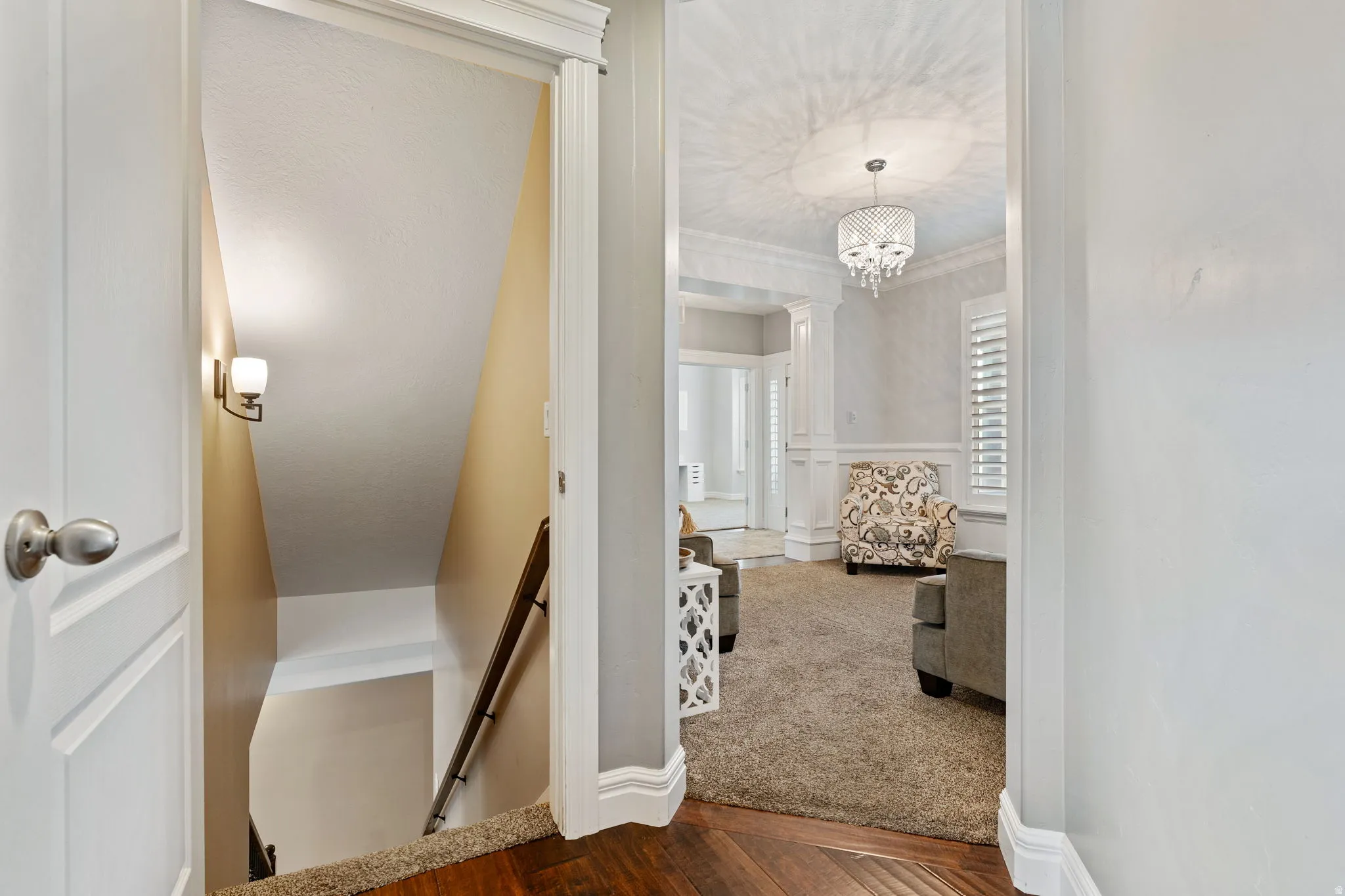 Stairway featuring crown molding, wood finished floors, carpet flooring, hanging lights, and ornate columns