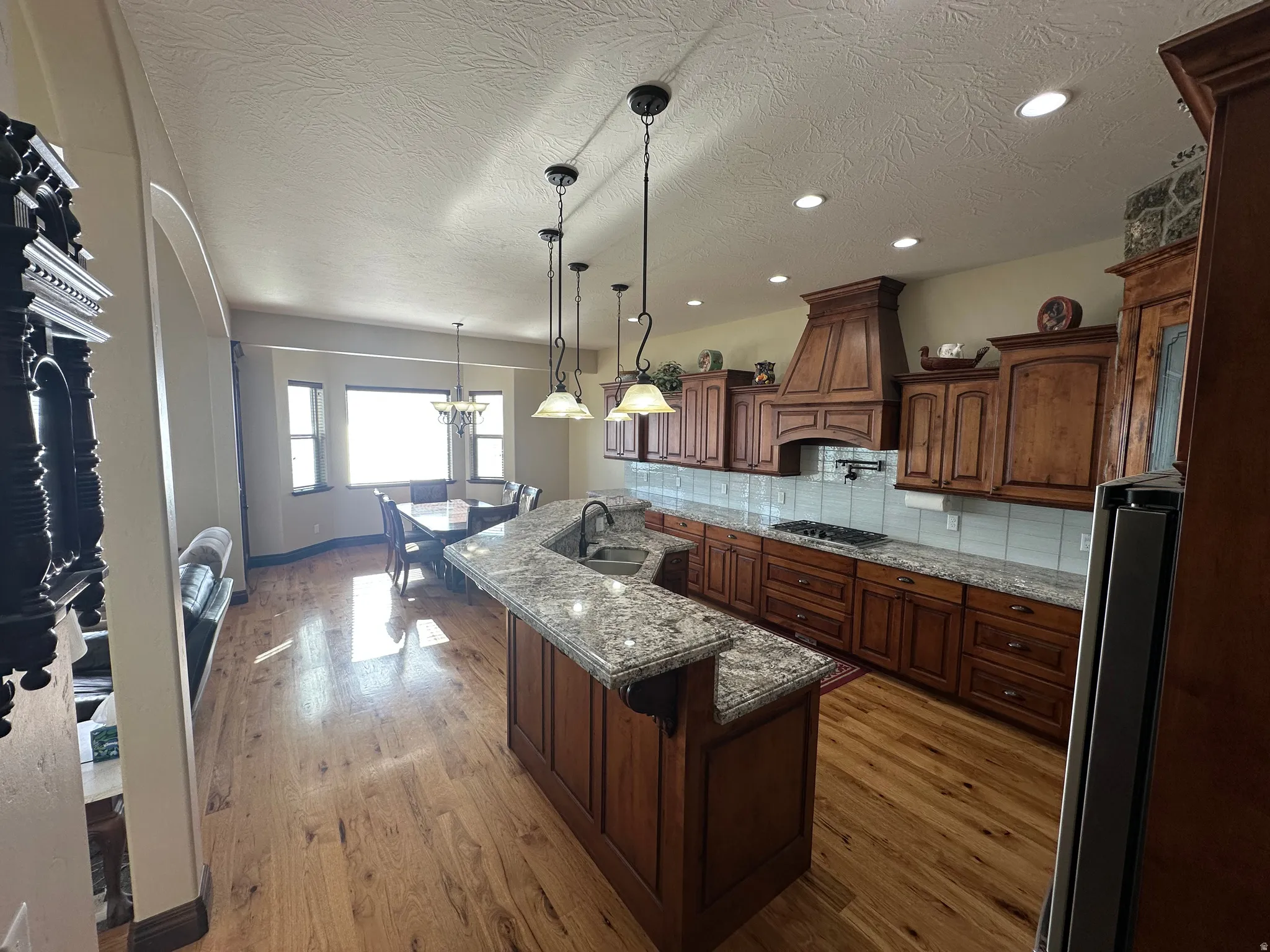 Kitchen featuring an island with sink, dark stone countertops, light wood-type flooring, tasteful backsplash, and a textured ceiling