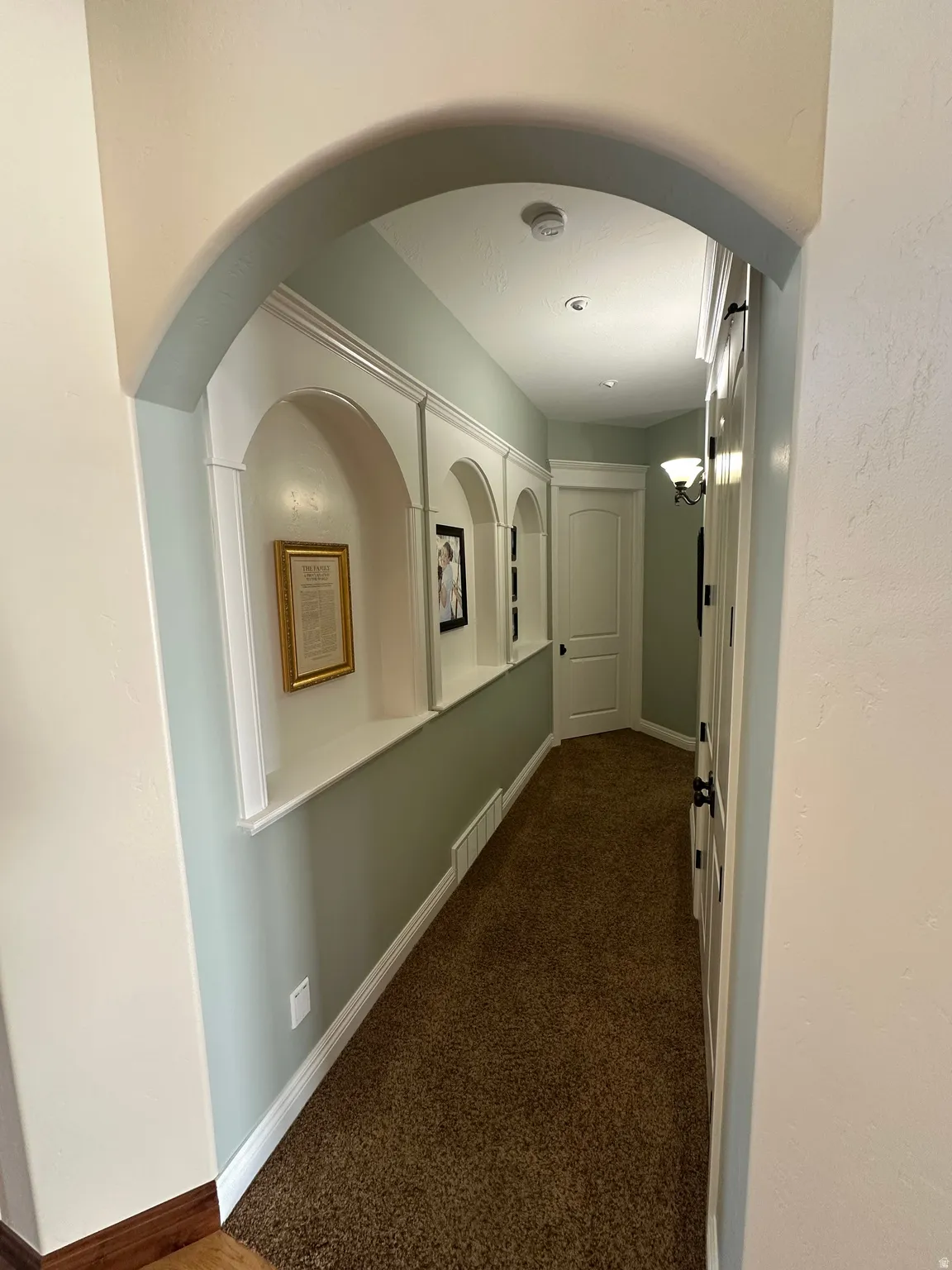 Hallway featuring arched walkways and dark carpet