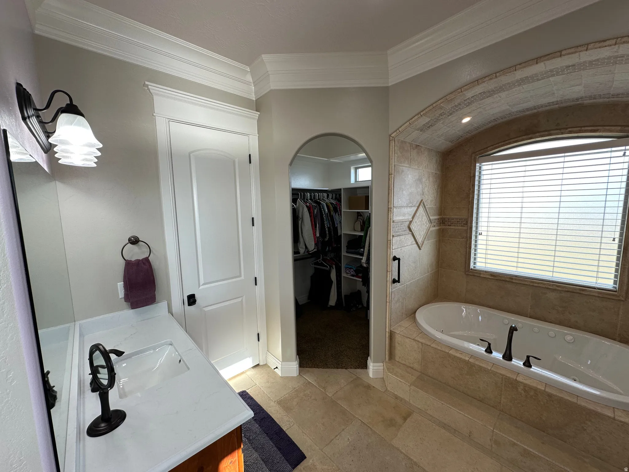 Bathroom with a bath, vanity, a walk in closet, ornamental molding, and light tile patterned flooring