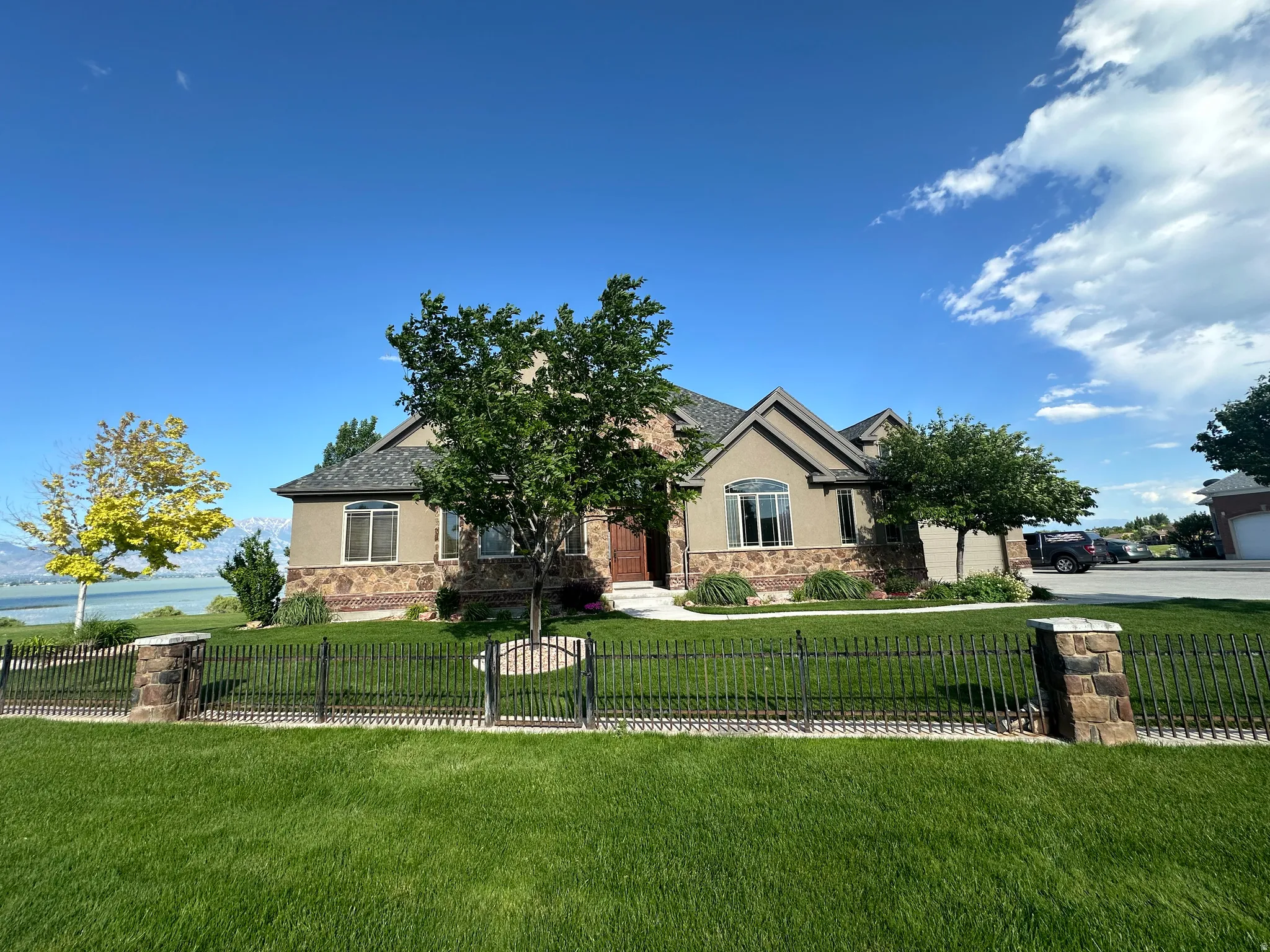 View of front of home with stone siding, stucco siding, a fenced front yard, a water view, and a gate