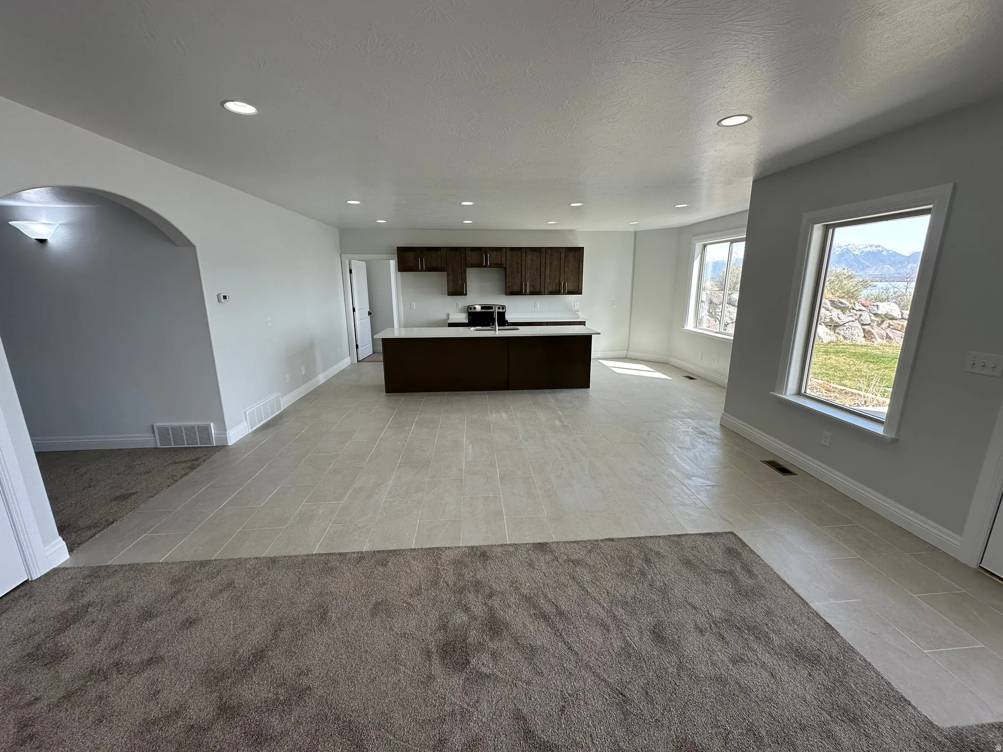 Kitchen featuring dark wood finish cabinetry, arched walkways, open floor plan, light countertops, and a kitchen island with sink