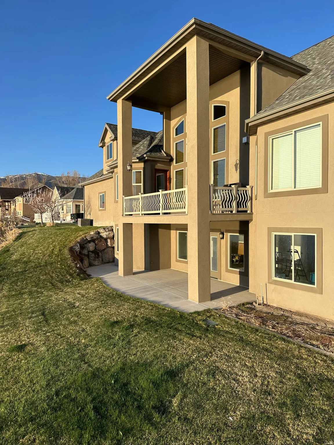 Back of property featuring a lawn, stucco siding, a balcony, and a patio