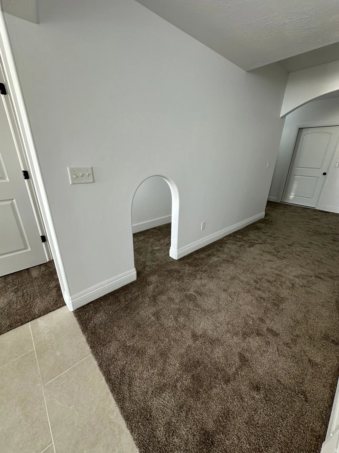 Unfurnished room with arched walkways, light colored carpet, and light tile patterned flooring