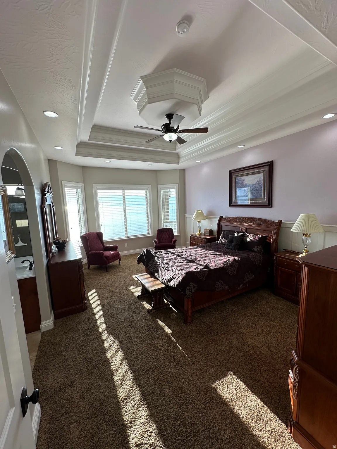 Master Bedroom with carpet floors, crown molding, a tray ceiling, a ceiling fan, and arched walkways