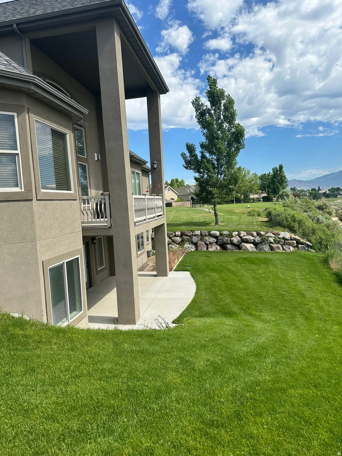 View of grassy yard with a patio and a balcony