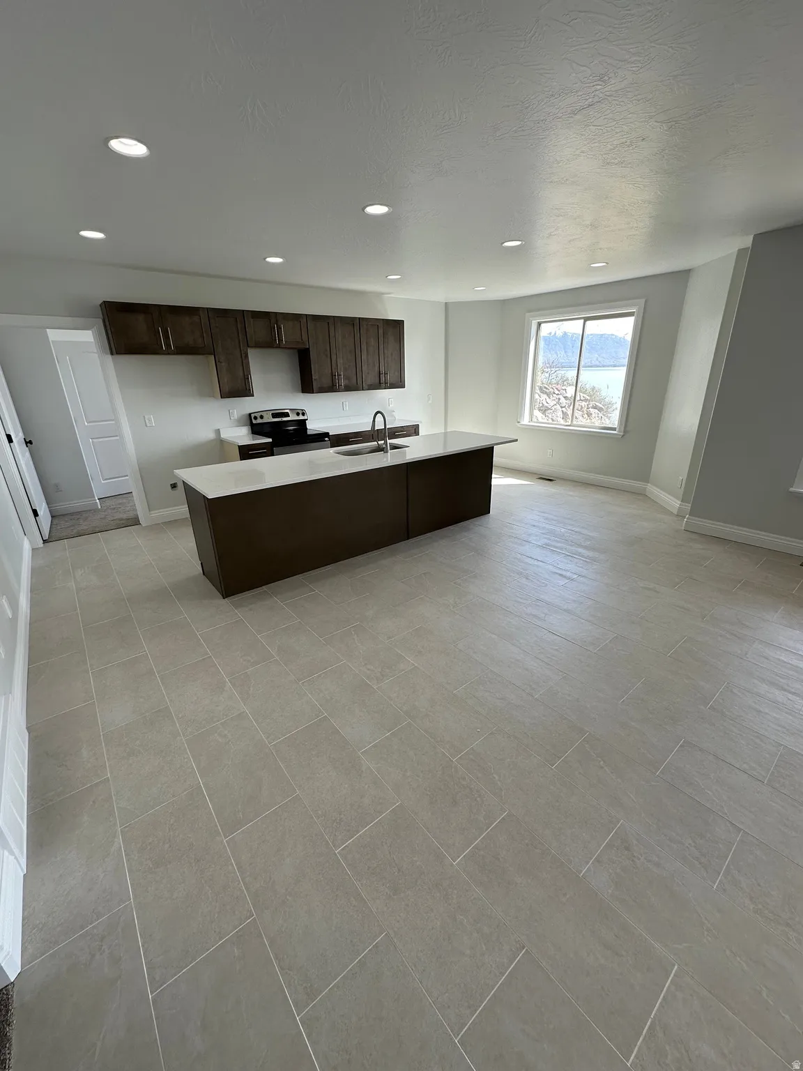 Kitchen featuring dark wood finish cabinets, an island with sink, stainless steel range with electric cooktop, and recessed lighting