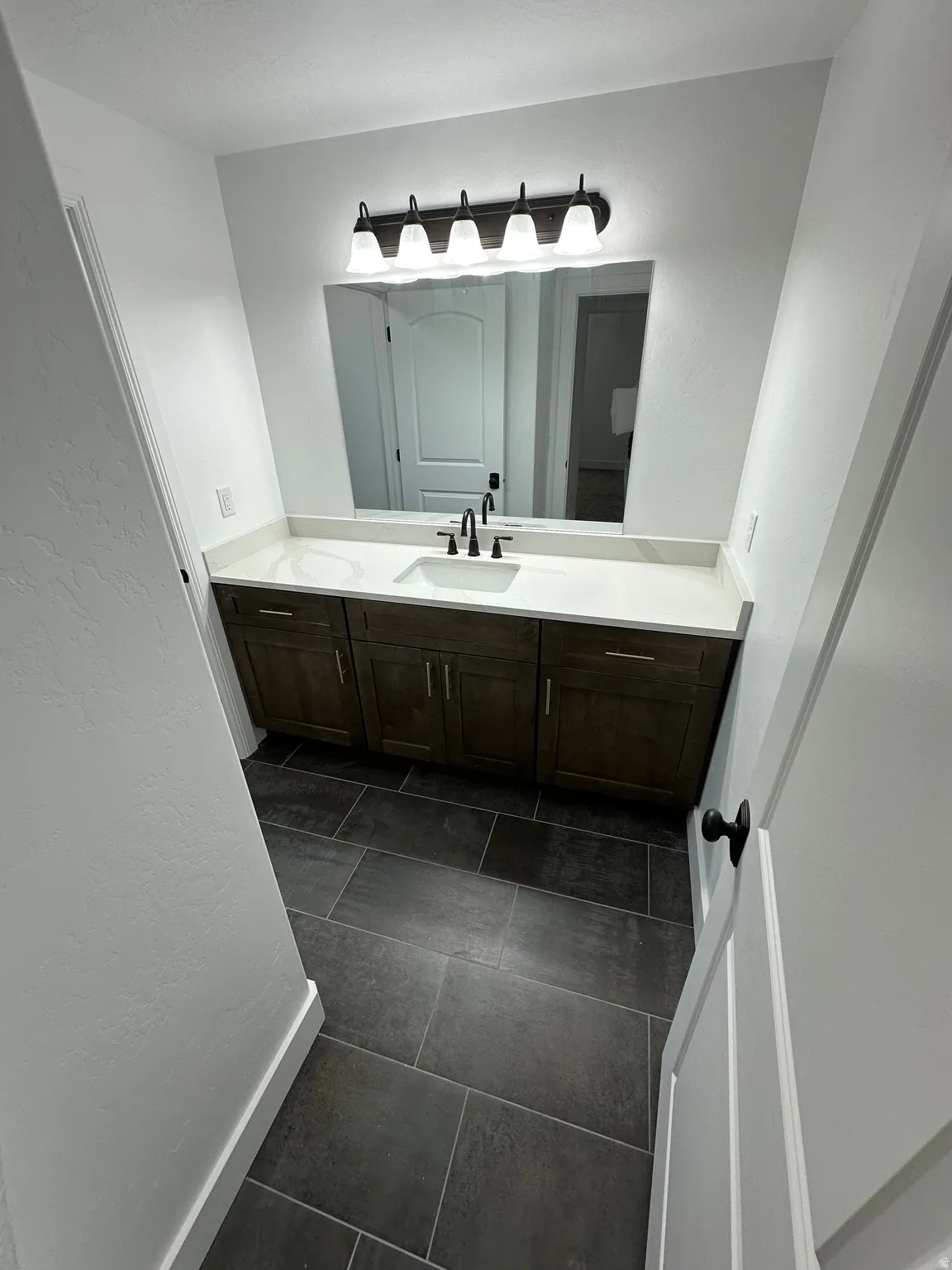 Bathroom featuring vanity, dark tile patterned flooring, and a textured wall