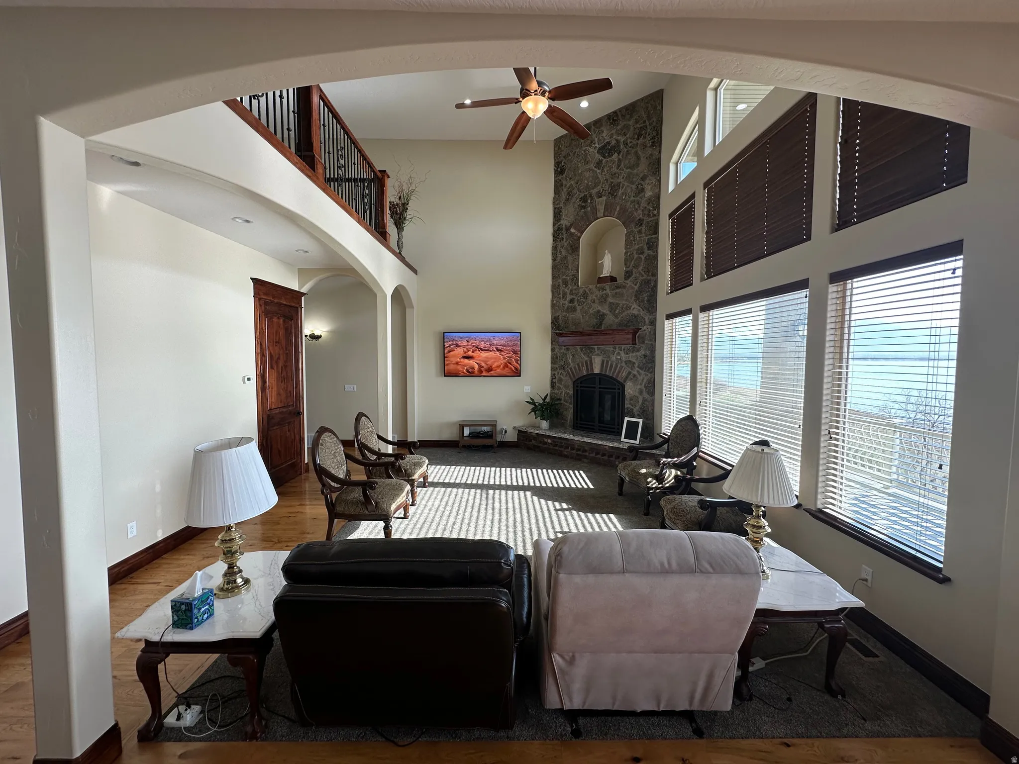 Living area featuring a stone fireplace, ceiling fan, wood finished floors, a high ceiling, and arched walkways