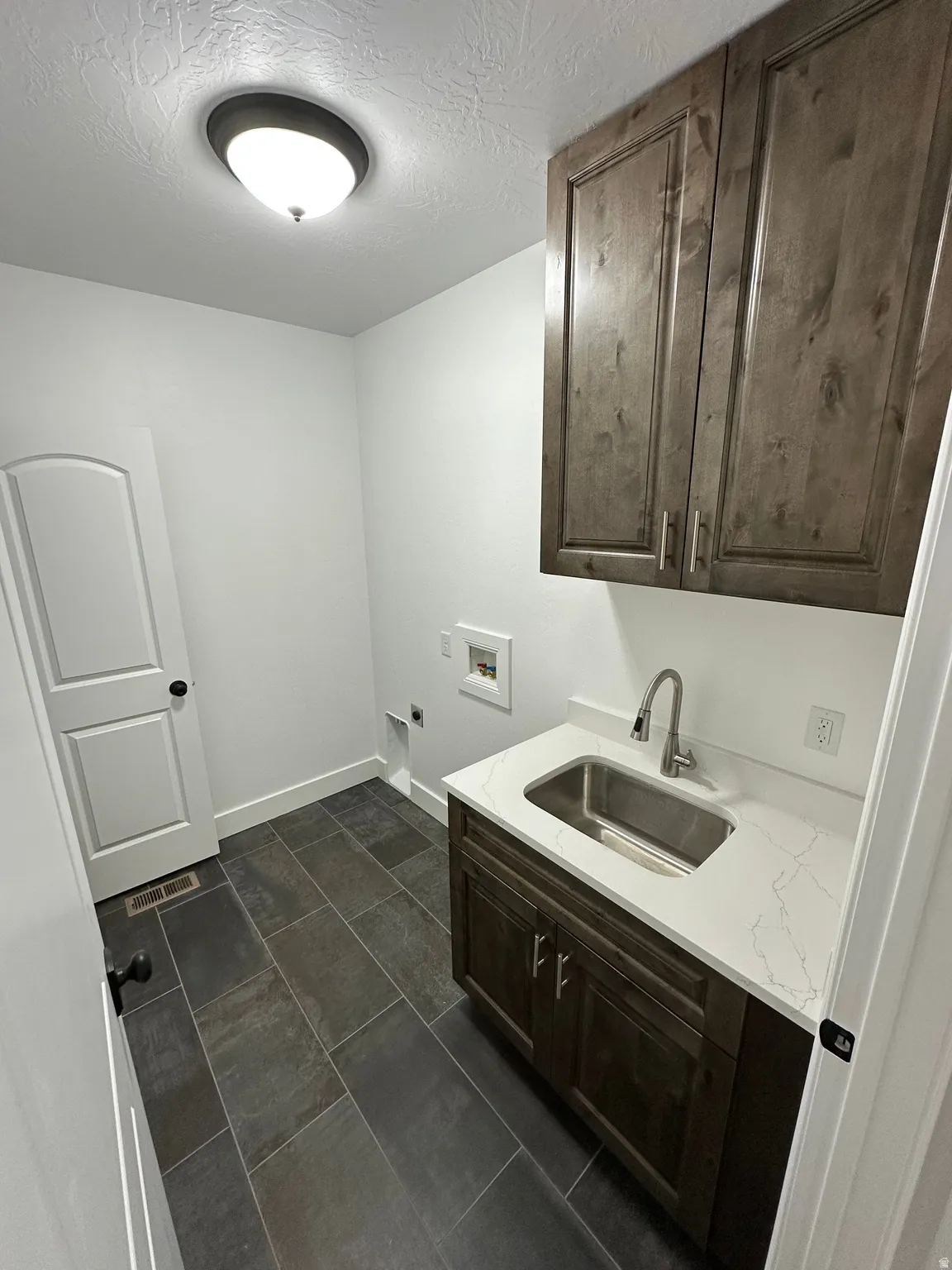 Laundry area with cabinet space, a textured ceiling, washer hookup, electric dryer hookup, and dark tile patterned floors