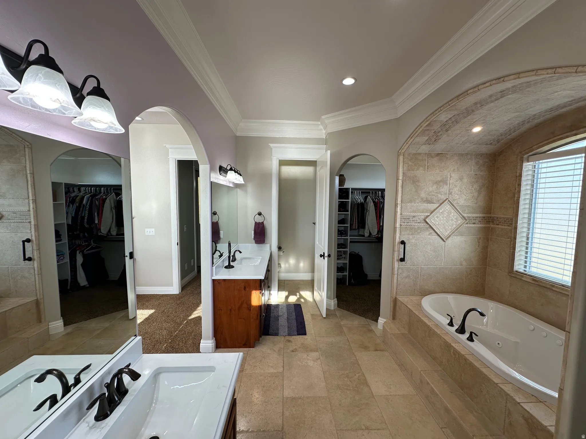 Bathroom featuring a spacious closet, two vanities, a jetted tub, ornamental molding, and recessed lighting
