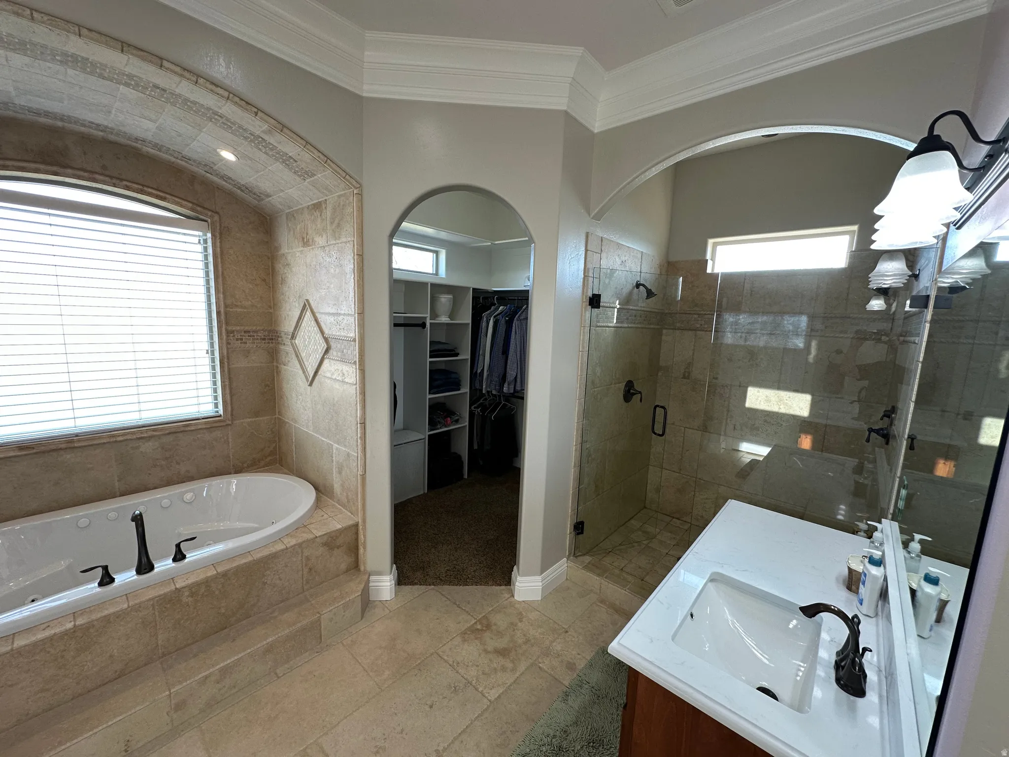 Bathroom with double vanity, a bath, a stall shower, a walk in closet, and light tile patterned floors