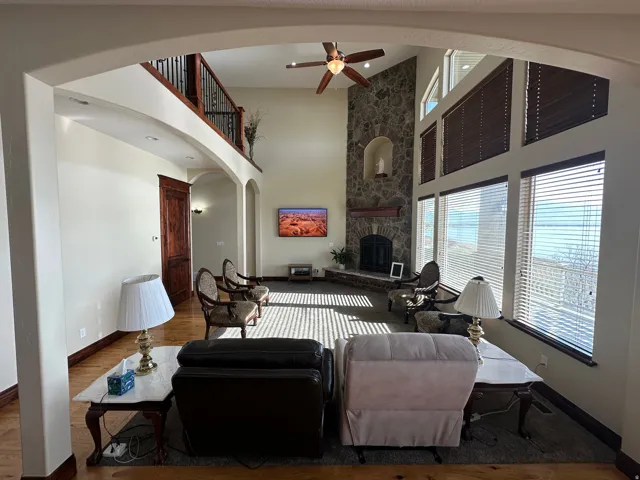 Living area featuring a stone fireplace, ceiling fan, wood finished floors, a high ceiling, and arched walkways