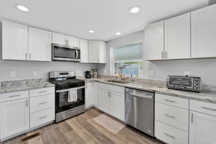 Kitchen with stainless steel appliances, white cabinets, light stone countertops, light wood-style floors, and recessed lighting